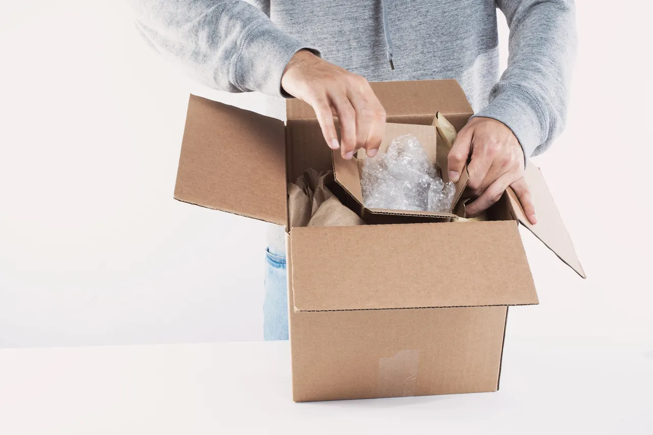 Hands packing an online order into a cardboard box